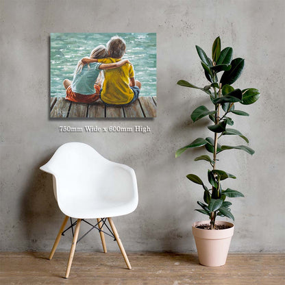 Wall art of two people sitting on a dock by a body of water, displayed on a wall with a white chair and potted plant.