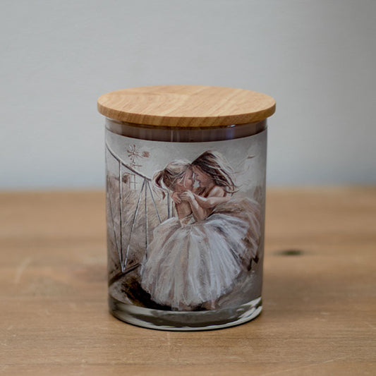 A vanilla scented wax candle with a cotton wick, placed in a clear glass jar with a wooden lid, featuring an illustration of a person on the jar.